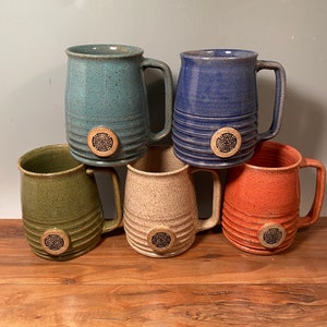 May include: Set of six ceramic mugs with a Celtic cross design. The mugs are in various colors, including green, blue, beige, and orange.