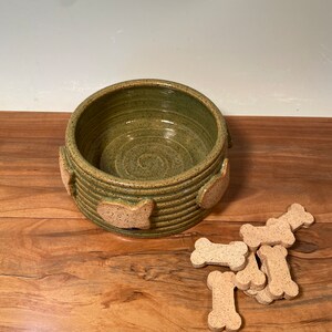 May include: A green ceramic pet bowl with a textured surface and paw print details. The bowl is filled with dog biscuits.