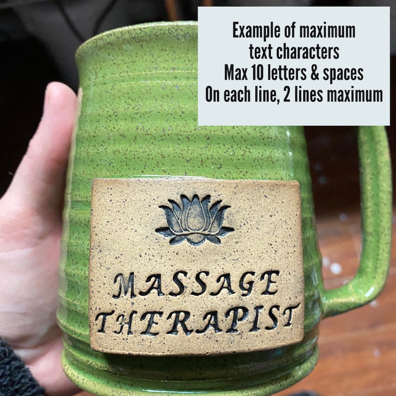 May include: Green ceramic mug with a brown rectangular label. The label has a black lotus flower design and the text "MASSAGE THERAPIST".