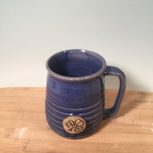 May include: A blue ceramic mug with a four-leaf clover design. The mug has a rounded body and a handle.