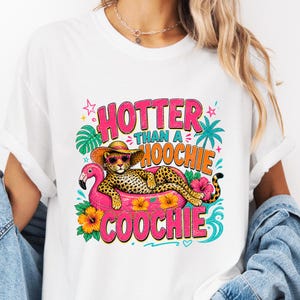 Könnte beinhalten: Weißes T-Shirt mit einem farbenfrohen Grafikdesign. Die Grafik zeigt einen Leoparden mit Sonnenbrille und Hut, der auf einem rosa Flamingo-Schwimmer liegt. Der Text lautet "HOTTER than a HOOCHIE COOCHIE".