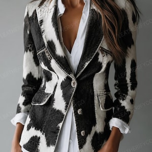 May include: A blazer featuring a black and white cow print pattern, long sleeves, a notched lapel, and a front button closure. The garment includes two horizontal zipped pockets on the chest and two flap pockets at the waist, worn over a white shirt.