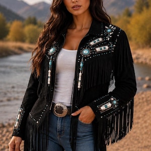 May include: A black jacket featuring long fringe detailing along the chest and sleeves. The garment is embellished with turquoise-coloured stones, white beads, and metallic accents on the shoulders, chest, and cuffs, paired with blue jeans.