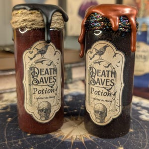 Peut inclure: Deux flacons cylindriques en verre étiquetés Death Saves Potion. Le flacon de gauche contient un liquide rouge foncé, de la ficelle beige et de la cire noire. Celui de droite contient un liquide noir, un cordon irisé et de la cire cuivrée.