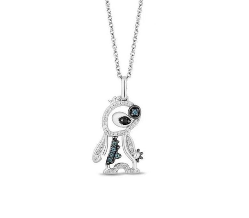 K&ouml;nnte beinhalten: Eine silberne Anh&auml;ngerkette mit einem stilisierten Kreaturendesign, das mit kleinen wei&szlig;en Diamanten besetzt ist. Die Kreatur hat ein dunkelblaues Auge, einen dunkelblauen, texturierten K&ouml;rperabschnitt und eine sternf&ouml;rmige Hand an einer Silberkette.