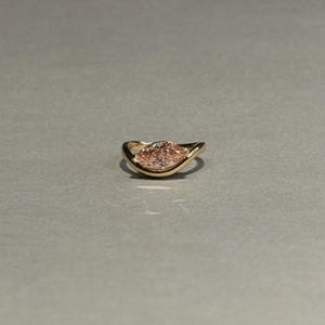 Könnte beinhalten: Ein Goldring mit einem pfirsichfarbenen Edelstein im Marquise-Schliff, der horizontal in eine glatte, geschwungene Metallschiene eingefasst ist, die den Stein umschließt und eine elegante, durchgehende Silhouette mit polierter Oberfläche bildet.