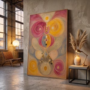 Puede incluir: Una gran pieza de arte mural rectangular enmarcada que presenta una composición abstracta de formas circulares arremolinadas y figuras orgánicas en tonos magenta, amarillo dorado y azul suave, dentro de un marco de madera clara.