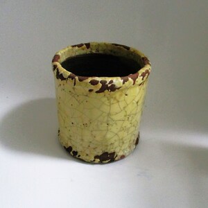 May include: A yellow ceramic planter with a crackled glaze and brown accents. The planter has a round opening and a cylindrical shape.