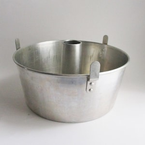 May include: A silver-colored angel food cake pan with a central tube and two handles. The pan is made of metal and has a wide, round shape. The handles are attached to the side of the pan.