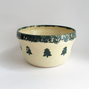 May include: A small, cream-colored ceramic bowl with a green rim and green tree designs.