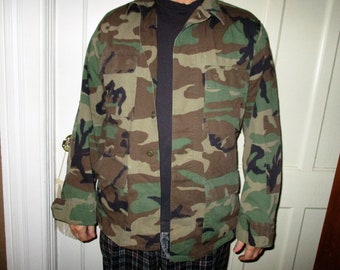 May include: A green, brown, and black camouflage jacket with a button-up front and two large pockets.