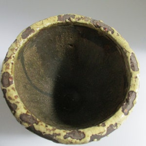 May include: A ceramic planter with a brown and yellow speckled glaze. The planter has a wide, round opening and a slightly rounded bottom.