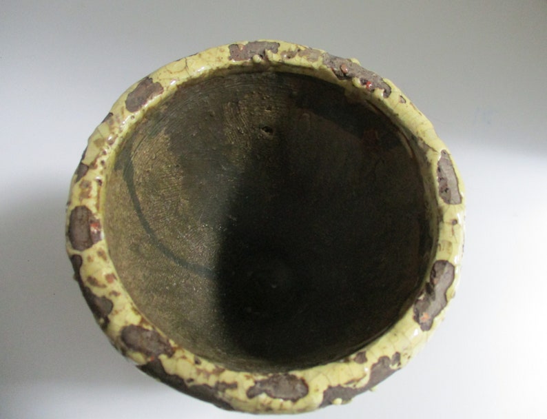 May include: A ceramic planter with a brown and yellow speckled glaze. The planter has a wide, round opening and a slightly rounded bottom.