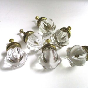 May include: A set of six clear glass cabinet knobs with a faceted, flower-like shape and a brass-toned metal base. Each knob features a central screw attachment, providing a functional hardware component for furniture or cabinetry doors and drawers.