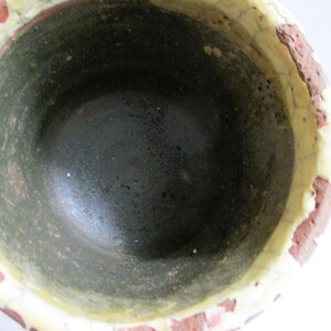 May include: A ceramic pot with a dark green interior and a white rim. The exterior is decorated with a red and white pattern.