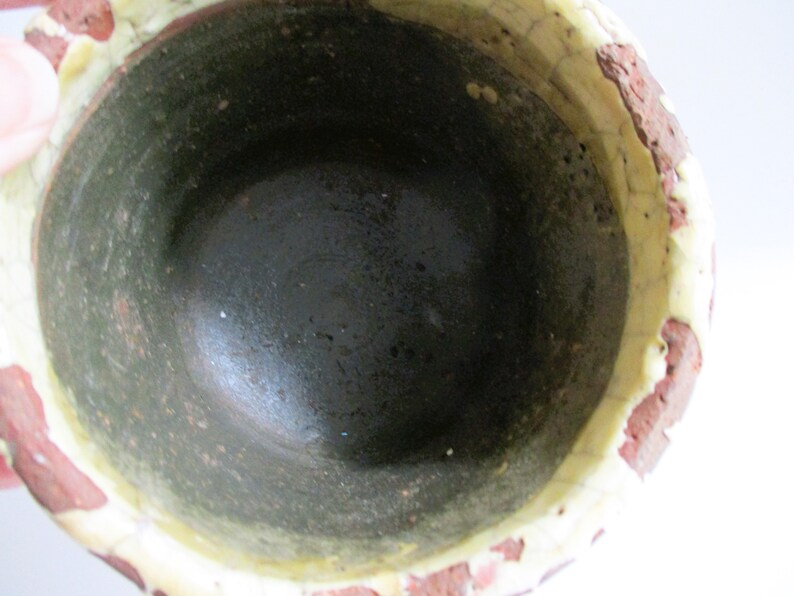 May include: A ceramic pot with a dark green interior and a white rim. The exterior is decorated with a red and white pattern.