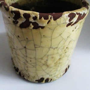 May include: A small, cream-coloured ceramic planter with a brown rim. The planter has a crackled glaze and a rustic look.
