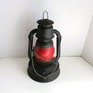 May include: A vintage black and red lantern with a handle. The lantern has a round red glass globe and a black metal frame. The base of the lantern has the number "100" printed on it.