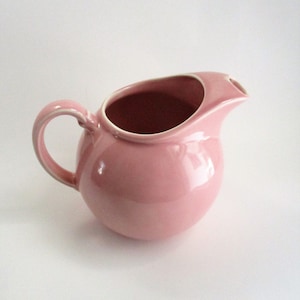 May include: A pink ceramic creamer pitcher with a rounded body and a curved spout.