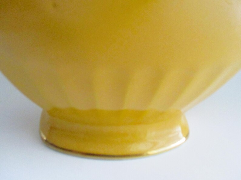 May include: A close-up of a yellow, vintage-style bowl. The bowl has a rounded shape with vertical ridges on the sides and a small, circular base. The base is trimmed with a gold-coloured band.