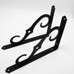 May include: Two black metal shelf brackets with a decorative scroll design. The brackets are angled and have a rustic finish.