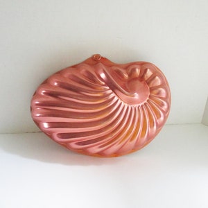 May include: A copper-colored, nautilus-shaped baking mold. The mold has a spiral design and a loop at the top. The color is a warm, metallic tone, and the mold appears to be made of metal.