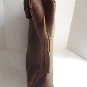 May include: A brown leather briefcase with a zipper closure and a handle. The briefcase is rectangular and appears to be vintage. The leather has a textured appearance.