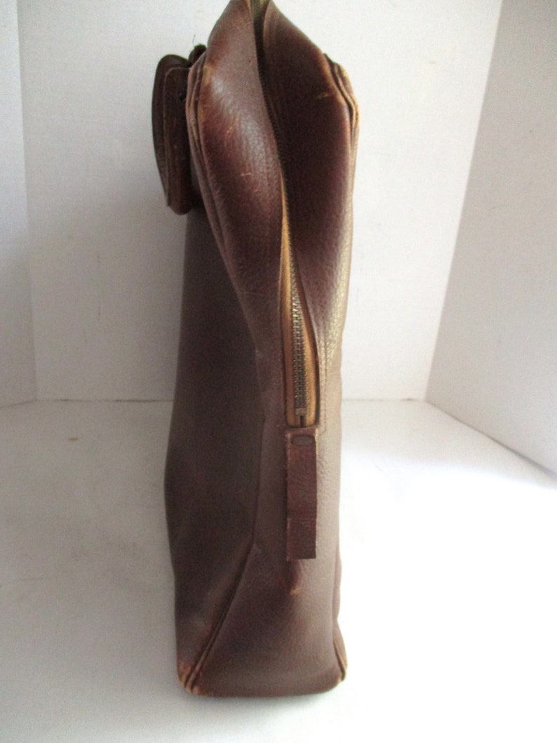May include: A brown leather briefcase with a zipper closure and a handle. The briefcase is rectangular and appears to be vintage. The leather has a textured appearance.