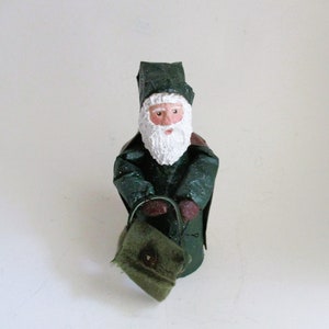 May include: A green Santa Claus figurine with a white beard and a green bag. The figurine is wearing a green hat and coat.