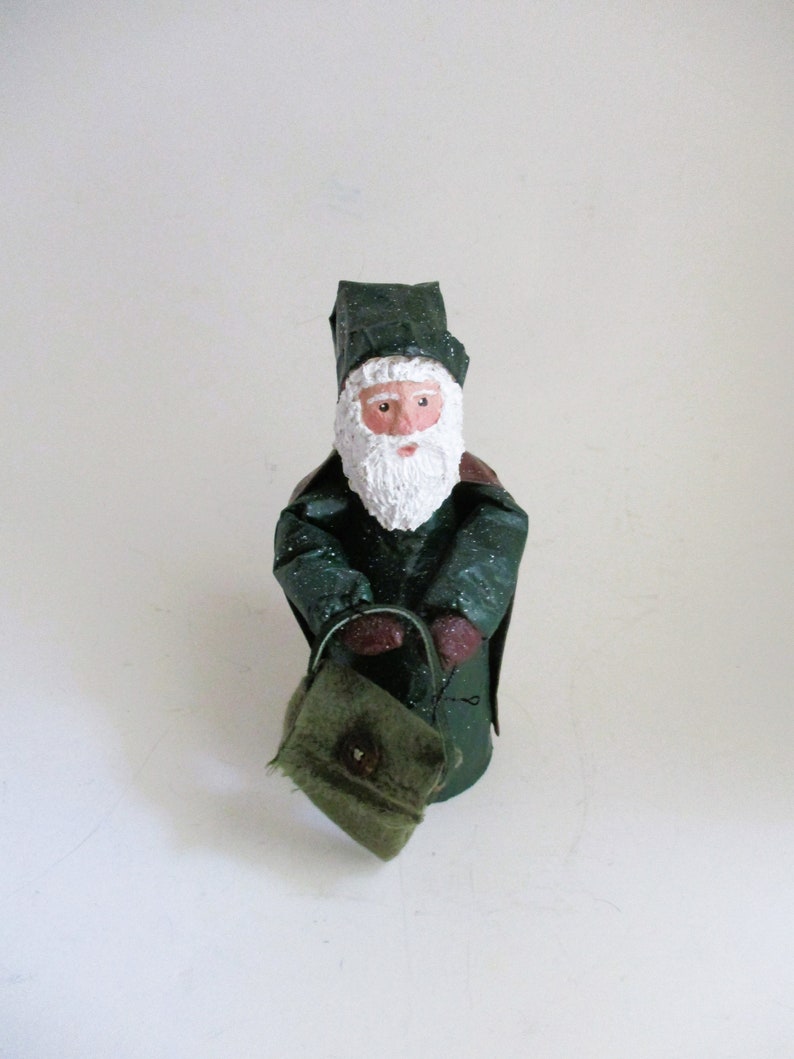 May include: A green Santa Claus figurine with a white beard and a green bag. The figurine is wearing a green hat and coat.