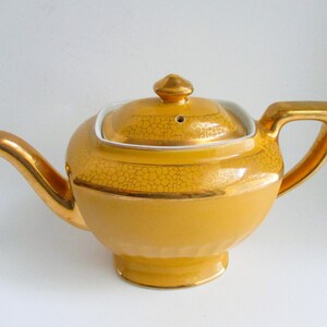 May include: A vintage yellow teapot with gold detailing on the handle, spout, and lid. The teapot has a rounded body and a square lid with a gold finial. The surface has a textured pattern.