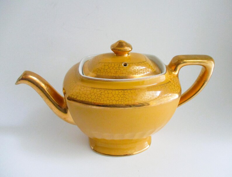 May include: A vintage yellow teapot with gold detailing on the handle, spout, and lid. The teapot has a rounded body and a square lid with a gold finial. The surface has a textured pattern.
