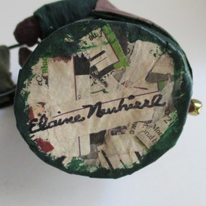 May include: A green and brown paper mache figurine with a signature that reads "Elaine Nuhifer" on the bottom.