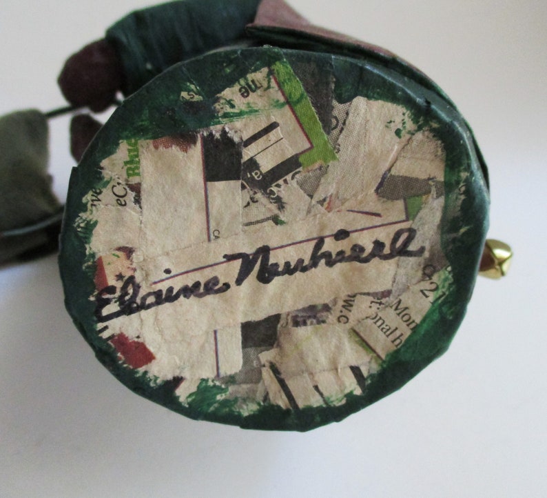 May include: A green and brown paper mache figurine with a signature that reads "Elaine Nuhifer" on the bottom.