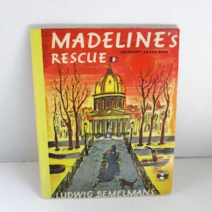 Puede incluir: Un libro antiguo de tapa dura titulado "Madeline's Rescue" de Ludwig Bemelmans. La portada presenta una ilustración de un edificio con una cúpula, una bandera y figuras caminando por un camino. El libro tiene lomo amarillo y portada roja y amarilla.