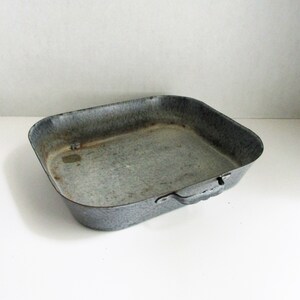 May include: A rectangular, vintage-style baking pan with a speckled gray and black enamel finish. The pan has rounded corners, a slightly flared rim, and a handle on one side. It is a kitchenware item.