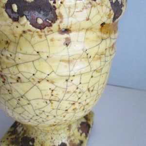 May include: A yellow ceramic planter with a square base and a cracked glaze. The planter has a distressed look with brown and white markings.