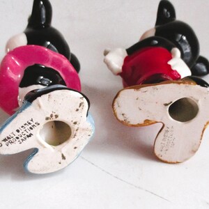 May include: Two ceramic Mickey Mouse figurines, one in red and one in pink, with black ears and shoes. The bottom of each figurine has the text "Walt Disney Productions Japan".