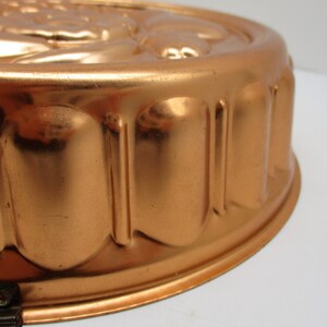 Puede incluir: Un molde redondo de cobre vintage para hacer un pastel o un postre. El molde tiene un borde acanalado y un dise&ntilde;o decorativo en la parte superior.