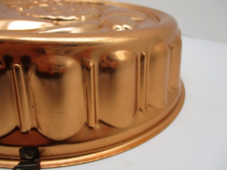 Puede incluir: Un molde redondo de cobre vintage para hacer un pastel o un postre. El molde tiene un borde acanalado y un dise&ntilde;o decorativo en la parte superior.