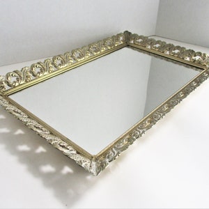 May include: A gold-colored rectangular tray with a mirrored surface and an ornate, decorative border.