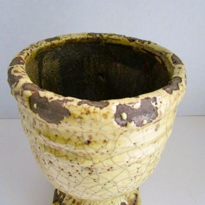 May include: A yellow ceramic planter with a crackled glaze and a brown rim. The planter has a wide, round opening and a square base.