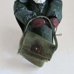 May include: A green fabric bag with a brown button and a brown strap. The bag is worn and has a frayed edge.