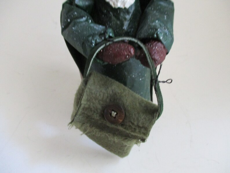 May include: A green fabric bag with a brown button and a brown strap. The bag is worn and has a frayed edge.