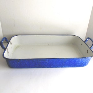 May include: A rectangular enamelware baking dish with a white interior and a vibrant blue exterior. The dish features two blue handles and is suitable for baking and serving. This vintage kitchenware adds a touch of retro charm.