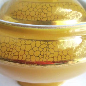May include: Close-up of a yellow ceramic teapot with a lid. The teapot has a gold, cracked pattern design and a white rim. The teapot is a light yellow colour and has a rounded shape.