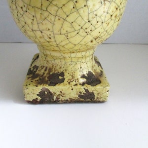 May include: A yellow ceramic vase with a crackled glaze and a square base. The vase has a brown and yellow color scheme.