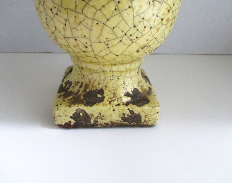 May include: A yellow ceramic vase with a crackled glaze and a square base. The vase has a brown and yellow color scheme.
