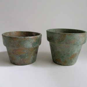 May include: Two terracotta flower pots with a green and copper patina finish. The pots are different sizes.