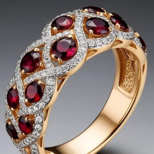 Peut inclure: Une bague en or dotée d'une bande tressée de style treillis, ornée de plusieurs pierres précieuses rondes rouge foncé. Le travail du métal est rehaussé de petites pierres claires serties pavé suivant les courbes, créant un aspect texturé.